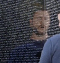 a man looking at a wall of names on a wall